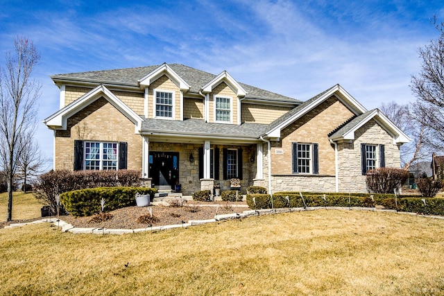 craftsman house with brick siding, a porch, a front yard, roof with shingles, and stone siding