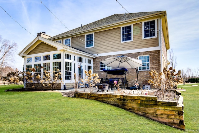 rear view of property with a chimney, a patio area, brick siding, and a lawn