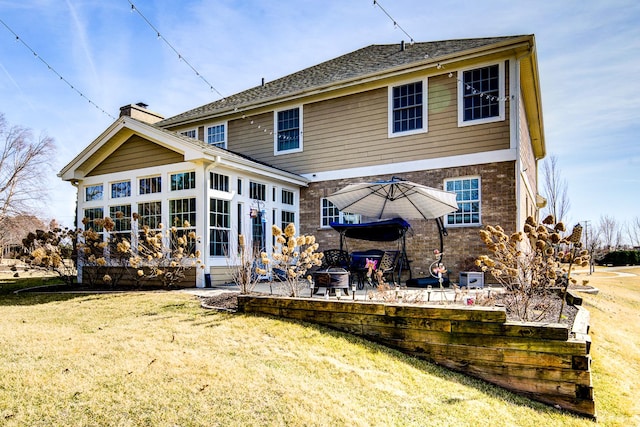 rear view of house featuring a patio area, a yard, a chimney, and brick siding