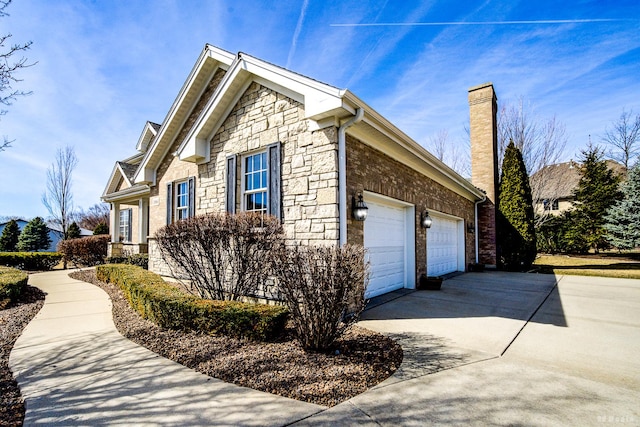 view of side of home with a garage, stone siding, driveway, and a chimney