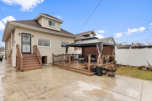 back of property featuring fence, roof with shingles, a wooden deck, a gazebo, and a patio area