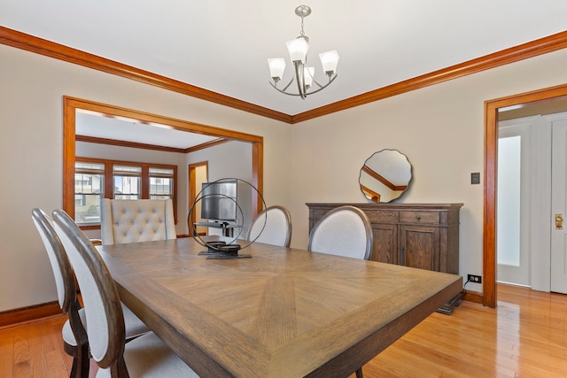 dining room featuring light wood finished floors, a notable chandelier, crown molding, and baseboards