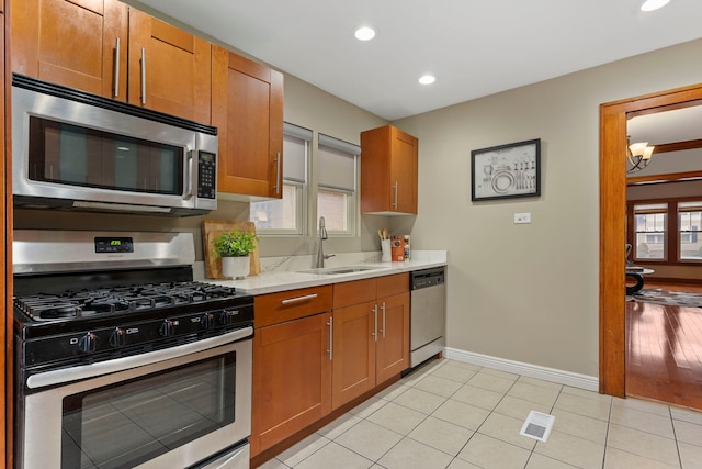 kitchen featuring baseboards, light tile patterned floors, brown cabinets, stainless steel appliances, and a sink