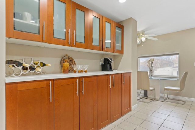 kitchen featuring glass insert cabinets, light tile patterned flooring, a ceiling fan, and light countertops