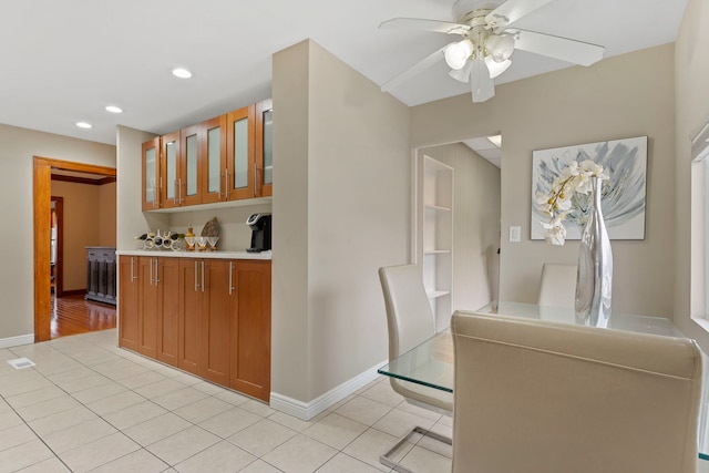 kitchen featuring light tile patterned floors, brown cabinetry, baseboards, light countertops, and glass insert cabinets