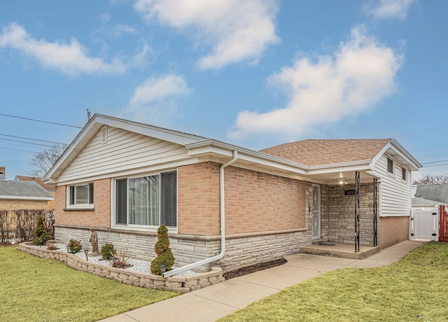 view of front of home featuring a shingled roof, stone siding, fence, a front lawn, and brick siding