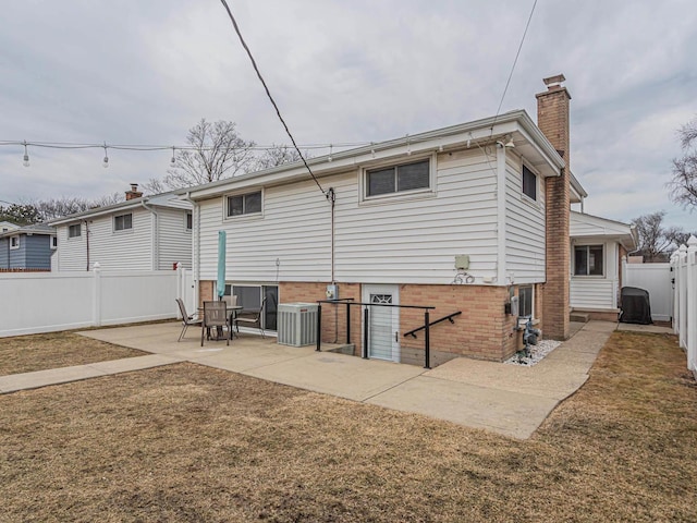 back of house featuring central AC unit, a fenced backyard, a chimney, a patio area, and brick siding