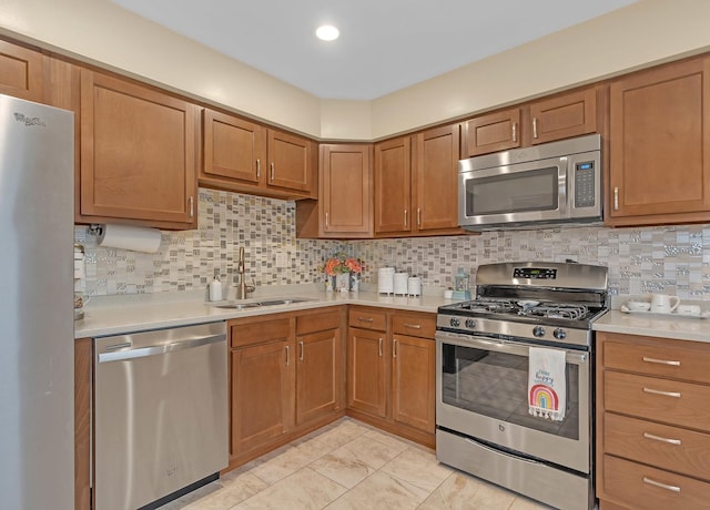 kitchen with brown cabinets, tasteful backsplash, light countertops, appliances with stainless steel finishes, and a sink