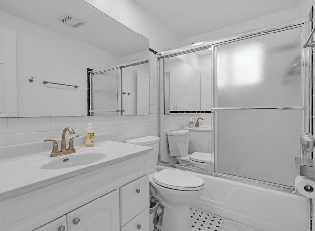 bathroom with visible vents, toilet, combined bath / shower with glass door, vanity, and tile walls