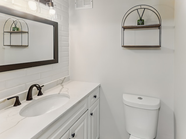 bathroom featuring backsplash, toilet, vanity, and visible vents