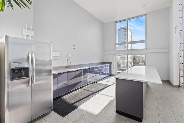 kitchen featuring a sink, stainless steel fridge, light countertops, and high vaulted ceiling