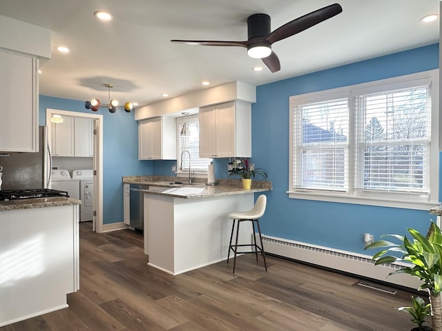 kitchen featuring dark wood-style floors, a breakfast bar area, a peninsula, washer and dryer, and a sink