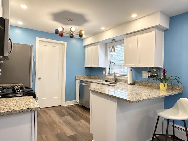 kitchen with a peninsula, a sink, appliances with stainless steel finishes, baseboard heating, and dark wood finished floors