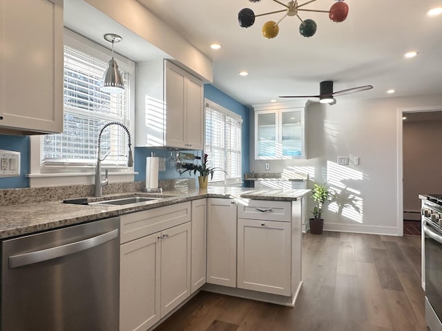 kitchen featuring appliances with stainless steel finishes, dark wood-type flooring, a peninsula, light stone countertops, and a sink