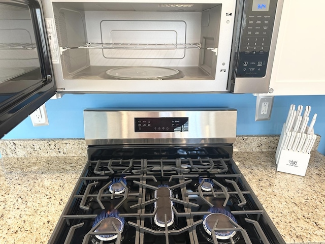 details with appliances with stainless steel finishes, white cabinetry, and light stone countertops