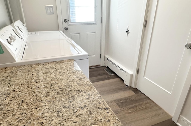 clothes washing area featuring dark wood-type flooring, a baseboard radiator, laundry area, and washing machine and clothes dryer