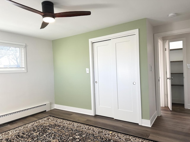 unfurnished bedroom featuring dark wood-type flooring, a ceiling fan, baseboards, baseboard heating, and a closet