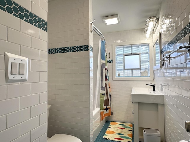 full bath featuring shower / bathtub combination with curtain, a sink, toilet, and tile walls