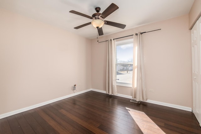 empty room featuring dark wood-style floors, a ceiling fan, visible vents, and baseboards