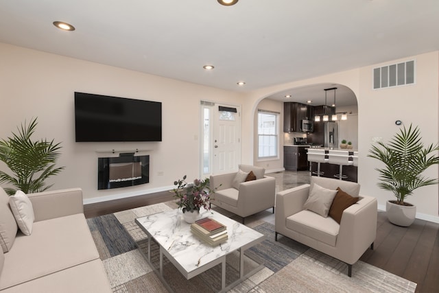 living room featuring arched walkways, visible vents, recessed lighting, and wood finished floors