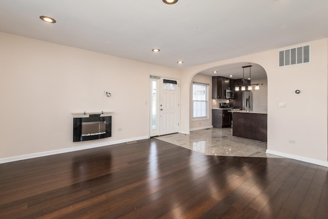 unfurnished living room with light wood finished floors, baseboards, visible vents, and arched walkways