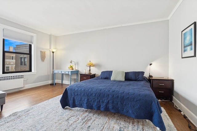 bedroom with radiator, crown molding, baseboards, and wood finished floors