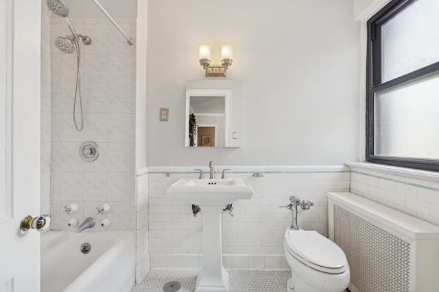 bathroom featuring a wainscoted wall, radiator heating unit, tile walls, and a wealth of natural light