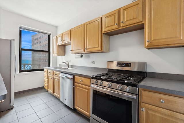 kitchen with light tile patterned floors, stainless steel appliances, a sink, baseboards, and dark countertops