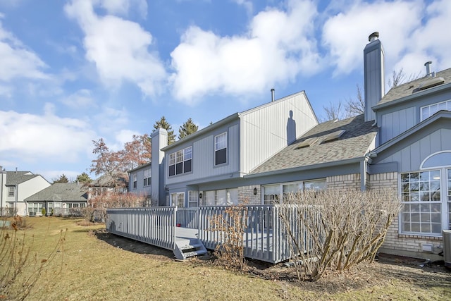 back of house featuring a yard, a chimney, a wooden deck, and a residential view