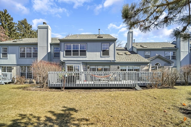 back of house featuring a chimney, a deck, a shingled roof, and a yard