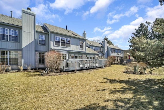 rear view of house featuring a chimney, a lawn, a residential view, a shingled roof, and a wooden deck