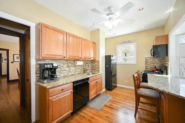 kitchen with black appliances, a sink, light wood finished floors, decorative backsplash, and ceiling fan