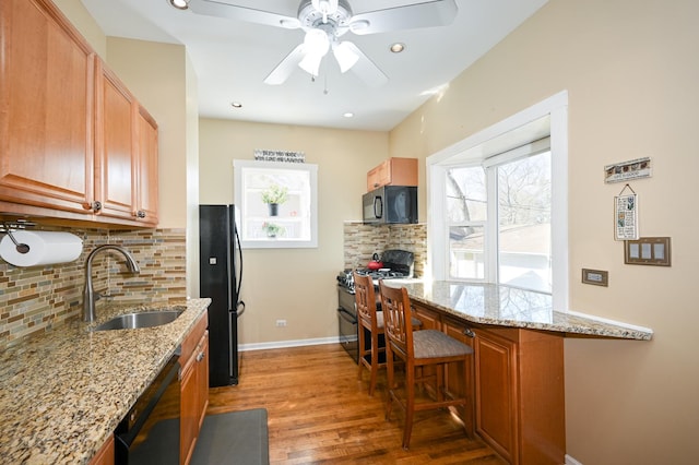 kitchen featuring light stone counters, baseboards, a sink, black appliances, and light wood-type flooring