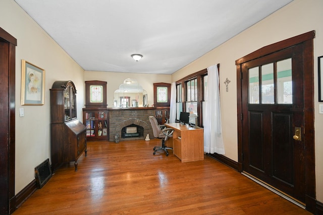 office space with visible vents, a brick fireplace, baseboards, and wood finished floors