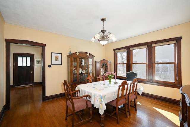 dining space with dark wood-type flooring, a notable chandelier, and baseboards