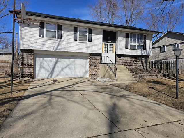 bi-level home featuring a garage, concrete driveway, brick siding, and fence