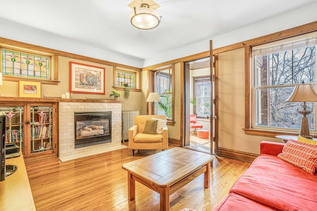 living room with a wealth of natural light, a brick fireplace, radiator heating unit, and wood finished floors