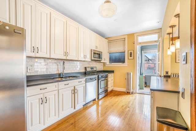 kitchen with a sink, light wood-style floors, appliances with stainless steel finishes, tasteful backsplash, and dark countertops