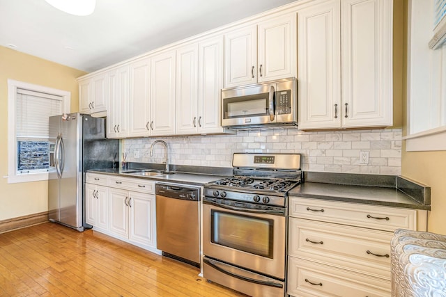 kitchen with tasteful backsplash, dark countertops, appliances with stainless steel finishes, light wood-style floors, and a sink