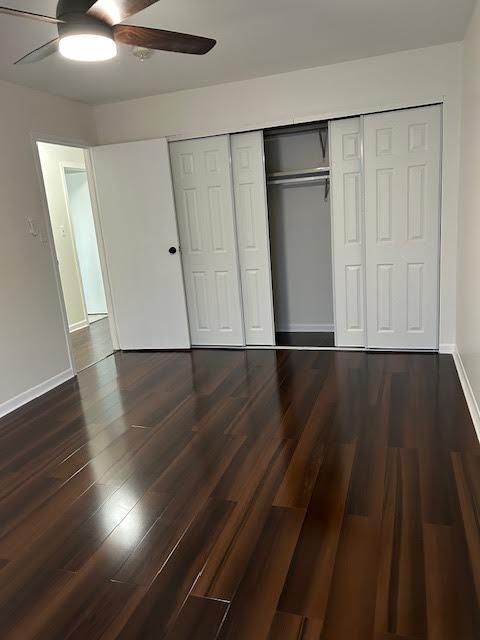 unfurnished bedroom with ceiling fan, a closet, dark wood finished floors, and baseboards