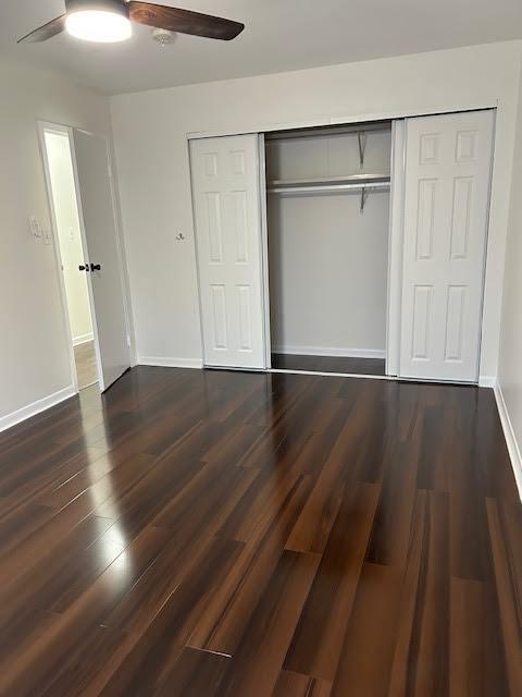 unfurnished bedroom featuring a ceiling fan, a closet, dark wood finished floors, and baseboards