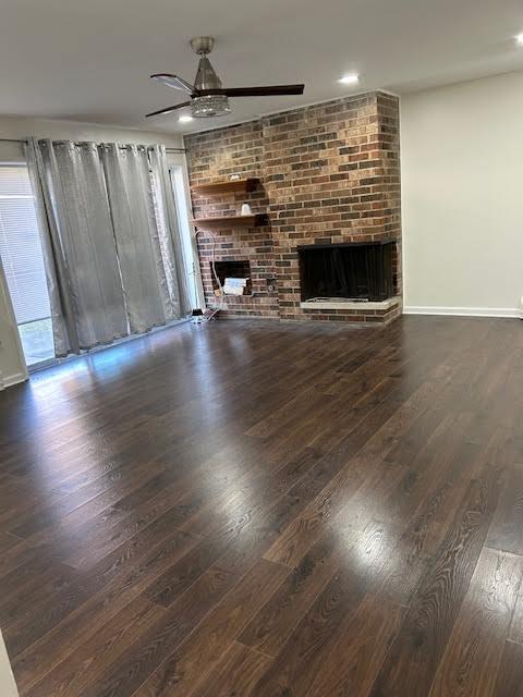 unfurnished living room featuring a brick fireplace, ceiling fan, baseboards, and wood finished floors