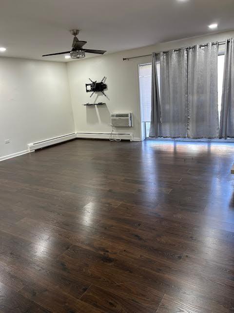 empty room with a ceiling fan, dark wood-style flooring, a wall mounted air conditioner, and plenty of natural light