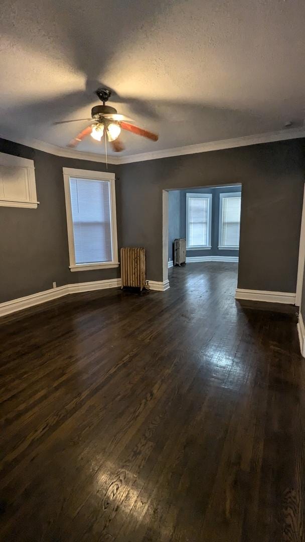 unfurnished living room featuring dark wood-style floors, radiator heating unit, baseboards, and crown molding