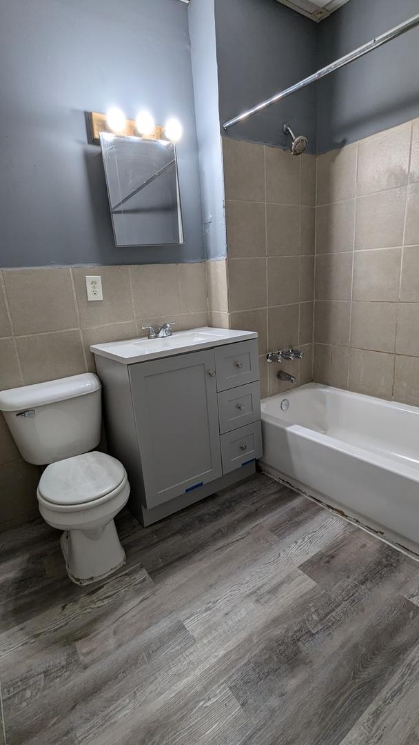 full bathroom with toilet, wood finished floors, bathtub / shower combination, vanity, and tile walls