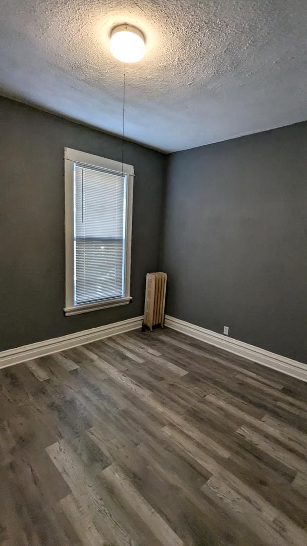 unfurnished room with radiator, baseboards, a textured ceiling, and dark wood-style flooring