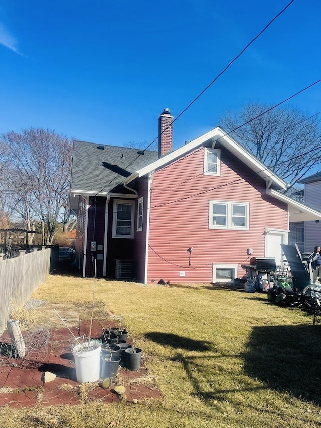 back of property featuring central AC, fence, a yard, a shingled roof, and a chimney