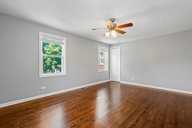 empty room with ceiling fan, dark wood-style flooring, visible vents, and baseboards