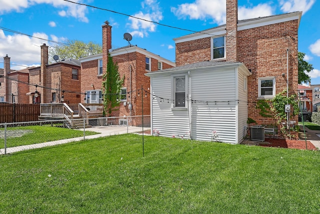 rear view of house featuring central air condition unit, brick siding, fence, and a yard