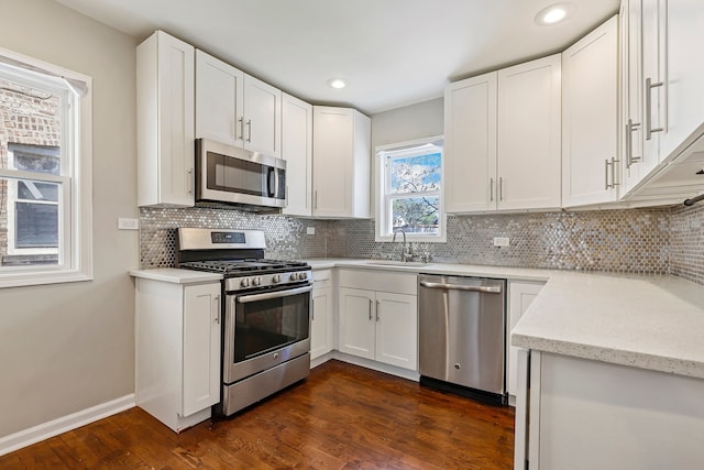 kitchen with tasteful backsplash, appliances with stainless steel finishes, dark wood-style flooring, white cabinetry, and a sink